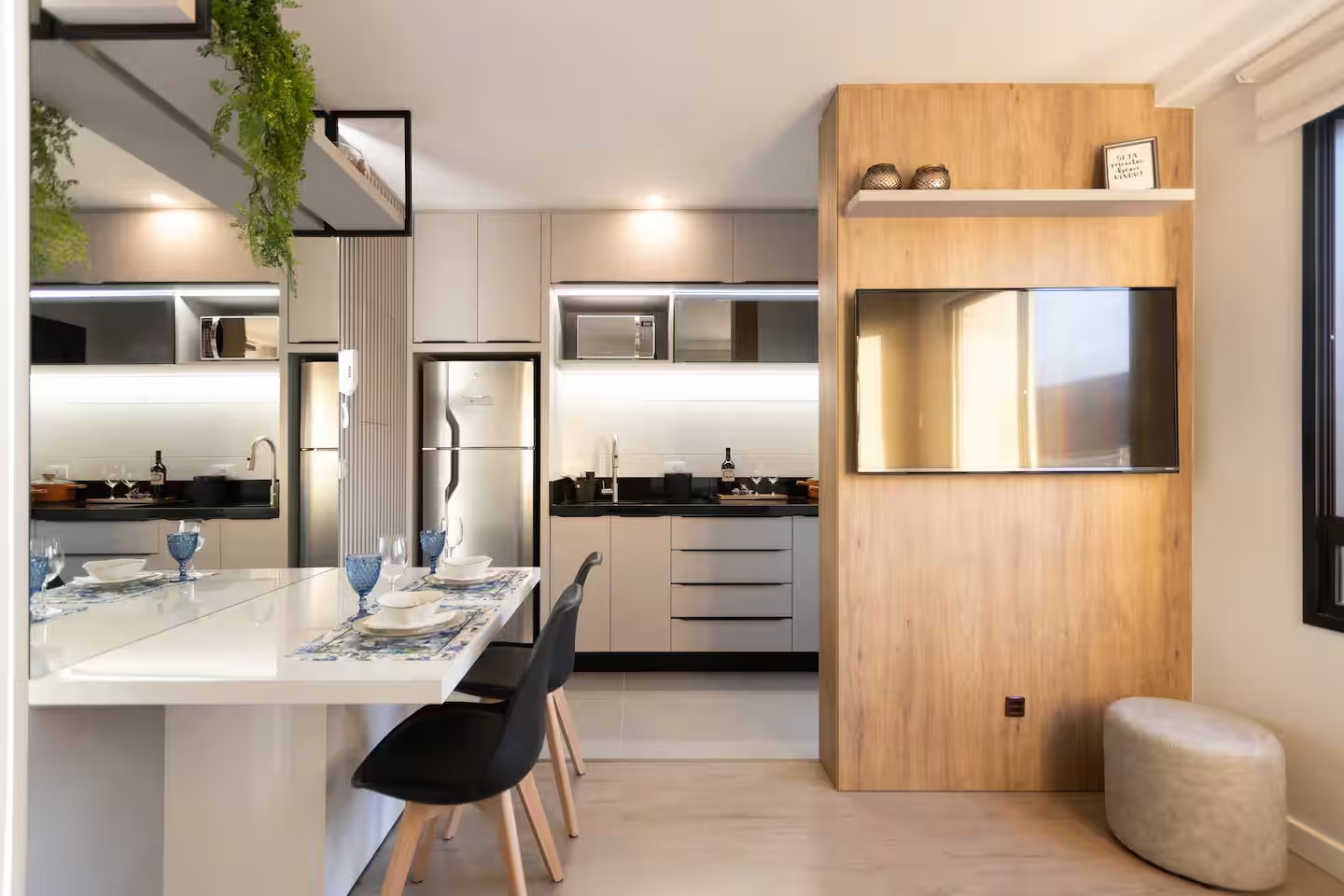 Studio com cozinha compacta, jantar e painel de TV em madeira